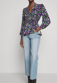 Blommig wrap-blus med djup V-ringning, långa utsvängda ärmar och peplummidja i lila, grönt och vitt. Kombinerad med ljusa jeans.