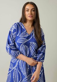 Vestido azul con un patrón de motivos de hojas blancas. Tiene un escote en V y mangas de tres cuartos, confeccionado en una tela texturizada.