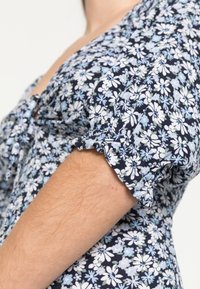 Vestido floral com fundo azul-marinho e flores brancas e azul claro, mangas curtas franzidas e detalhe de botão no decote.