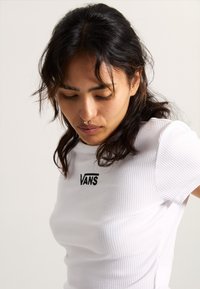 Hvid ribbet t-shirt med korte ærmer, udstyret med et sort "VANS" logo på brystet. Stoffet har et blødt, tekstureret udseende.