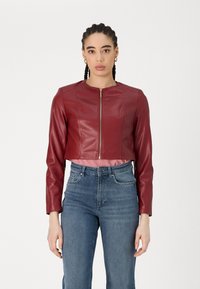 Giacca di pelle rossa cropped con maniche lunghe, chiusura con zip e dettagli cuciti, abbinata a jeans chiari a vita alta.