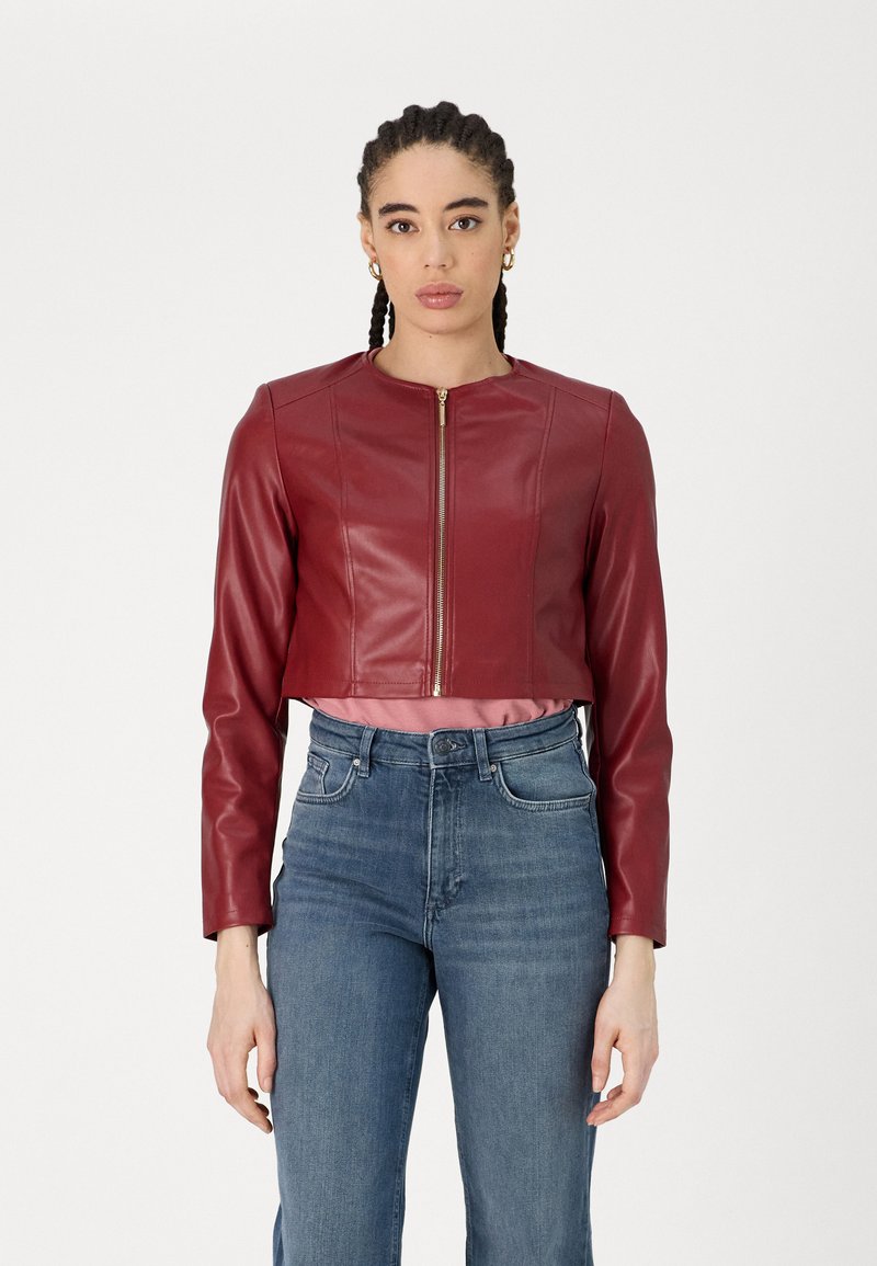 Giacca di pelle rossa cropped con maniche lunghe, chiusura con zip e dettagli cuciti, abbinata a jeans chiari a vita alta.