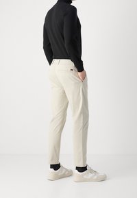 Beiga tapered byxor med elastisk midja, detalj med bakficka, kombinerat med vita sneakers och en svart långärmad tröja.