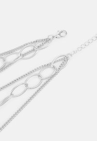 Bijoux en chaîne en argent avec des maillons ovales entrelacés et une finition texturée. Équipé d'un fermoir en forme de homard et de plusieurs brins de chaîne de longueurs variées.