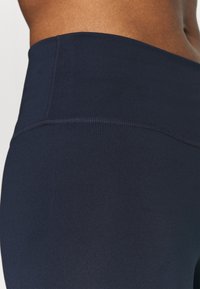 Granatowe legginsy z wysokim stanem, wykonane z gładkiego, elastycznego materiału z subtelnymi detalami w szwie. Dostosowują się komfortowo do kształtu ciała.