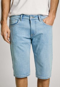 Shorts de mezclilla azul claro con un ajuste relajado, que presentan un diseño clásico de cinco bolsillos y lazos para cinturón. Textura suave y corte recto.