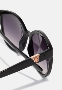 Black sunglasses with gradient purple lenses, oversized cat-eye shape, and a metallic rose gold accent on the temple. Smooth plastic texture.