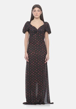 Donna in piedi che indossa un lungo vestito nero con macchie floreali rosse, maniche corte a sbuffo e scollo a cuore arricciato.