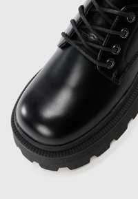 Black leather ankle boot with a rounded toe, textured rubber sole, and metal eyelets for laces. Smooth finish with a sturdy design.