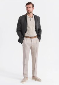 Conjunto masculino que incluye un blazer gris oscuro, una polo beige, pantalones beige claros y zapatos tipo slip-on en color crema. Destaca un detalle del cinturón en cuero marrón.
