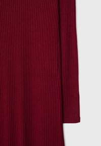 Tissu en tricot côtelé à manches longues de couleur bordeaux profond avec un détail de texture verticale.