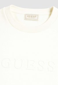 Felpa bianca con scollatura rotonda. Presenta un logo "GUESS" testurizzato sul davanti. Tessuto morbido e liscio con collo a costine.