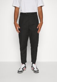 Svarta byxor med rak passform, med slät front, bältesömmar och sidofickor. Matchat med vit t-shirt och svarta sneakers.