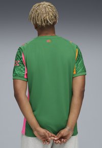 Kortärmad sporttröja i grönt, med rosa, orange och mönstrade detaljer på ärmarna. Texten "CITY" i orange vid halsringningen.