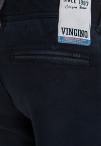 Mörkblå denimbyxor med en bakficka, som har en synlig märklapp där det står "VINGINO" och ytterligare textdetaljer.