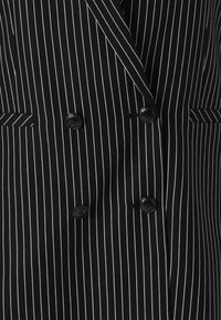 Black pinstripe blazer with double-breasted front, notched lapels, and two flap pockets. Features black buttons and a smooth fabric texture.
