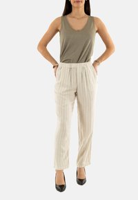 Grijze tanktop gecombineerd met lichtgekleurde gestreepte broek. De broek heeft een elastische tailleband en taps toelopende pijpen. Zwarte hoge hakken maken de outfit compleet.
