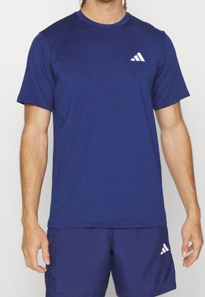 Homme portant un t-shirt de sport bleu marine uni et un short assorti, tous deux avec de petits logos Adidas blancs sur la poitrine et la cuisse.