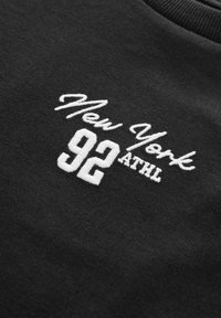 Juodas džemperis su balta siuvinėta užrašu „New York 92 ATHL.“ Minkšta medžiaga, apvaliu kaklu ir įpjovimu.