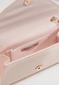 Intérieur de sac rose clair au toucher satin, avec une doublure lisse, des ferrures dorées et une étiquette indiquant "ANNA FIELD". Comprend une petite poche.