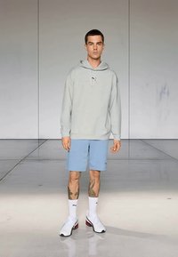 Svetlo šedá mikina s kapucňou, svetlo modré šortky, biele tenisky s červenými akcentmi a biele ponožky. Hladká tkanina, voľný strih, minimálne značkovanie.