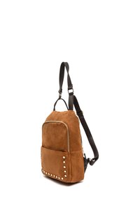 Sac à dos en daim brun avec des bretelles réglables sombres, poche zippée à l'avant et rivets dorés le long des bords de la poche sur fond blanc.