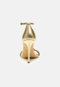 Scarpa con tacco alto dorata, con punta affilata, cinturino alla caviglia e finitura metallica. Presenta un design elegante e tacco a stiletto.