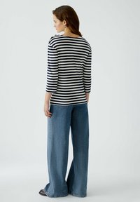 Gestreiftes Langarmoberteil in Marineblau und Weiß, kombiniert mit hochgeschnittenen, weiten blauen Jeans. Hat eine entspannte Passform und eine weiche Textur.