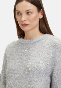 Grau strukturierter Plüschpullover mit texturierter Oberfläche, der vorne verstreute dekorative Perlenakzente und einen runden Ausschnitt aufweist.