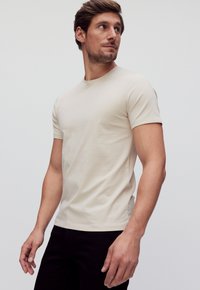 Beige katoenen T-shirt met een ronde halslijn en korte mouwen. Strak ontwerp met een zachte textuur en minimalistische stijl. Draagt het met zwarte broeken.