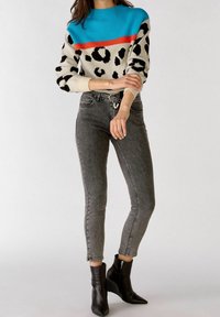 Sweter dzianinowy w niebieskie i czerwone paski oraz czarny wzór w panterę; zestawiony z szarymi rurkami i czarnymi botkami z długim noskiem.