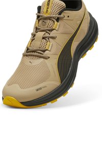 Beige trail running shoe with a textured mesh upper, black accents, yellow outsole, and reinforced toe cap. Features traditional lacing.