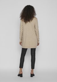 Beige lång kofta i mjukt stickat material med ribbade ärmslut och nederkant. Kombinerad med eleganta svarta läderbyxor och klackskor med blockklack.