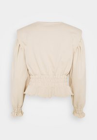 Blusa de color crema con mangas abullonadas, cintura ajustada con bordes fruncidos y una textura suave y lisa.