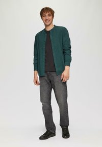 Teeffarbene Button-up-Hemd mit entspannter Passform, über einem schwarzen T-Shirt getragen, kombiniert mit verblassten schwarzen Jeans und schwarzen Sneakers. Einfaches Design, keine sichtbaren Muster.