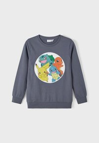 Sweatshirt gris avec des poignets côtelés, arborant un motif circulaire de quatre personnages de bande dessinée : Pikachu, Bulbizarre, Salamèche et Carapuce.