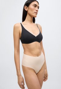 Μαύρο σουτιέν με βαθύ ντεκολτέ και μπριτζ στα γήινα χρώματα με ψηλή μέση, και τα δύο κατασκευασμένα από απαλό ύφασμα. Ο σχεδιασμός διαθέτει διακριτική αντίθεση χρωμάτων στις άκρες.