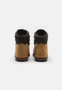 Bottines en daim marron avec des accents noirs, dotées d'un bout rond, d'un design à lacets et de semelles en caoutchouc texturé. Détail de couture visible.