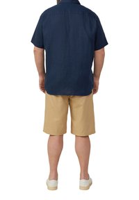 Marineblaues Kurzarmhemd mit Kragen, kombiniert mit beigen Shorts. Leichter Stoff, lockere Passform und einfaches Design. Weiße Sneakers runden den Look ab.