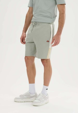 Mann trägt hellgraue Sportshorts mit weißen und beigen Seitenpanelen, kombiniert mit weißen Socken und klobigen weißen Sneakers.