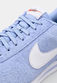 Gaiši zila samta brīvā laika apavu, ar teksturētu virsmu, baltu ādas swoosh logo, plakaniem auklām un mīkstinātu mēlīti ar izšūtu zīmola etiķeti.