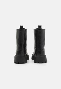Botine negre din piele, cu o textură netedă, talpă groasă neagră și mânere la spate pentru a fi ușor de încălțat.