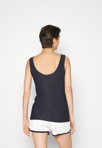 Top sem mangas azul-marinho feito de uma mistura de algodão, com um design de costas baixas; usado com calções brancos com bordas em azul-marinho.