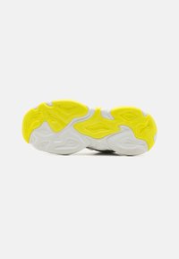 Suela de zapatilla con un diseño texturizado en blanco y amarillo vibrante, con una forma curva y un logo en relieve para mayor tracción.