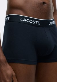 Navy blue cotton boxer briefs with an elastic waistband marked "LACOSTE" in white. Features a fitted design and smooth texture.