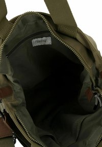 Oliven grøn taske med lynlåsåbning, stofindvendig og en lille lynlås-lomme. Justerbare stropper og læderdetaljer tilføjer finesse.