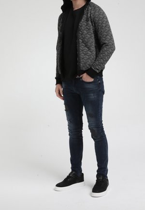 Quilted grey bomber jacket with hexagonal pattern, black sleeves, paired with distressed dark denim jeans and black sneakers with white soles.