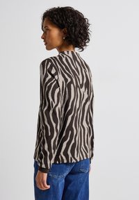 T-shirt à manches longues beige avec des rayures zèbres noires, avec un col rond et une coupe décontractée, associé à un jean en denim bleu.