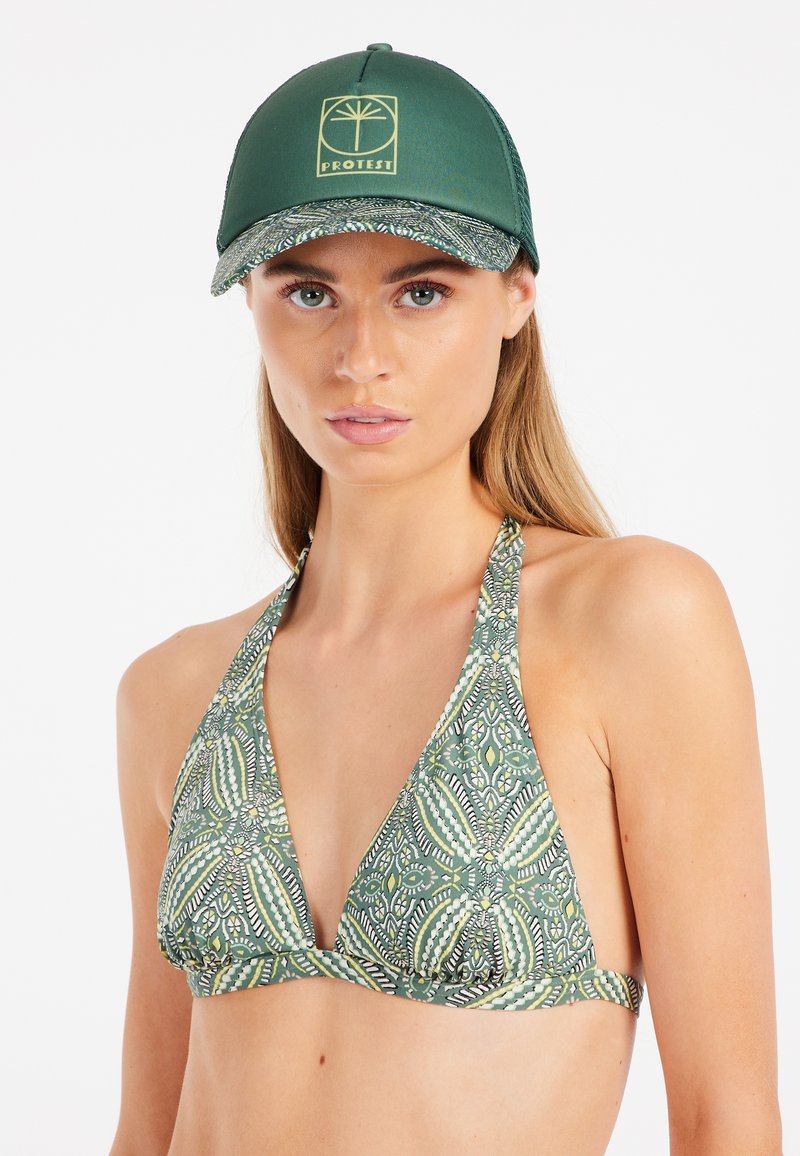 Zeleni bikini s uzorkom, halter neck dizajnom i tankim trakama. Sadrži cvjetni i lišćasti uzorak, uparen sa zelenom kapom.