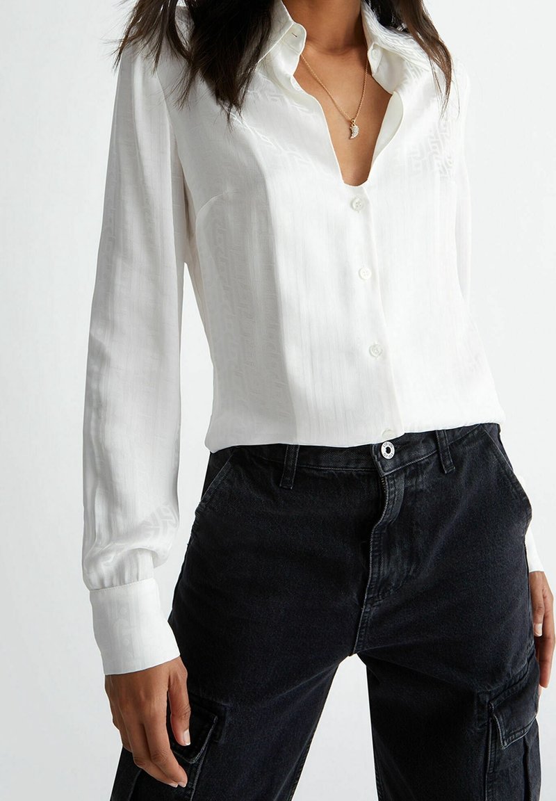 Camicia bianca a maniche lunghe con scollatura a V profonda, caratterizzata da un sottile motivo testurizzato, abbinata a pantaloni cargo neri a vita alta.